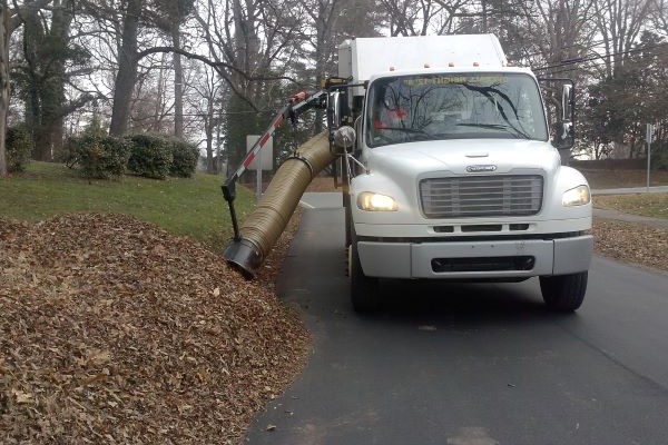 Leaf truck vacuuming loose leaves alongside a neighborhood street