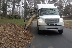 Leaf truck vacuums loose leaves on the side of a neighborhood street