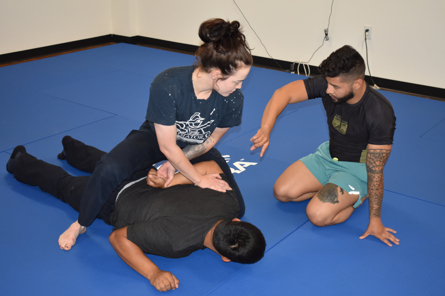 Two officers practice jiu jitsu with another officer providing instruction